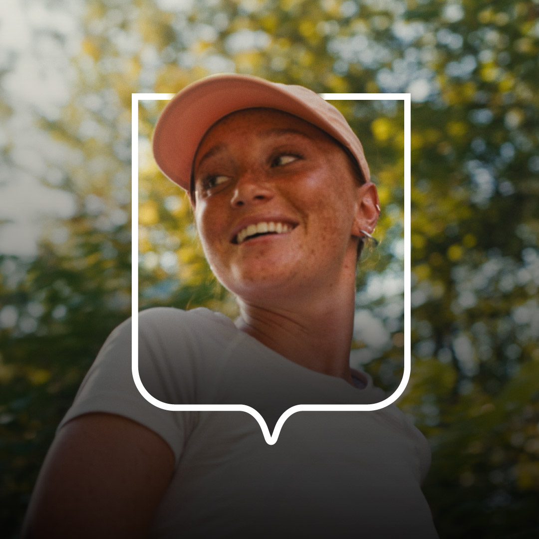 Une jeune adulte aux accents roux joggue en nature entourée de feuillage vert. Elle porte un casquette, la tête tournée vers la gauche. Sa tête est accentué par un blason ligné blanc de l'Université Laval.